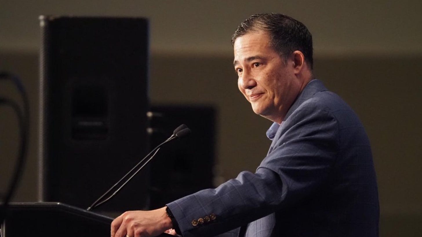 A man stands at a podium looking over to one side. A man stands at a podium looking over to one side.