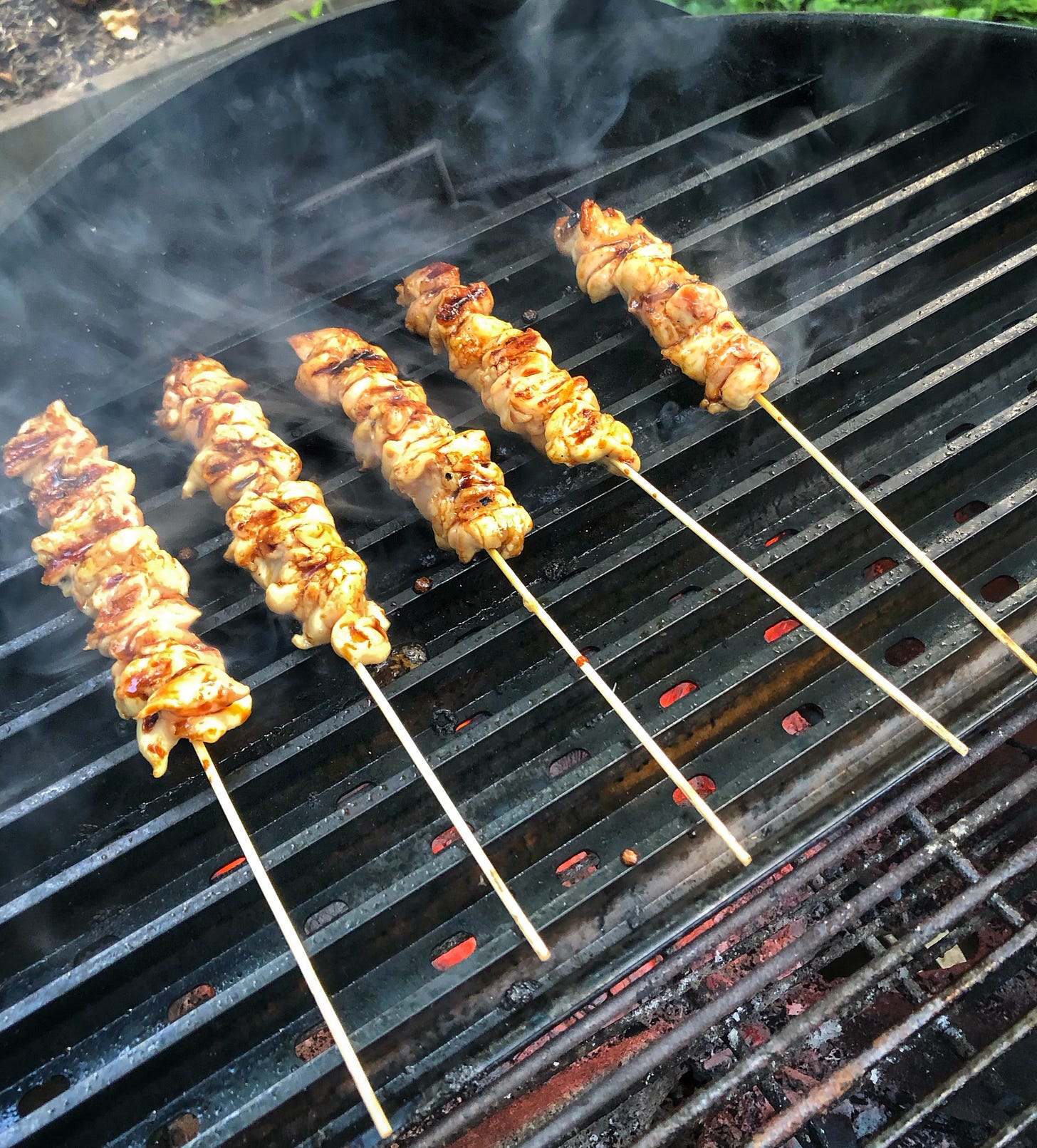 Skewers of chicken grilling on the ridged side of Grill Grates placed over a charcoal grill