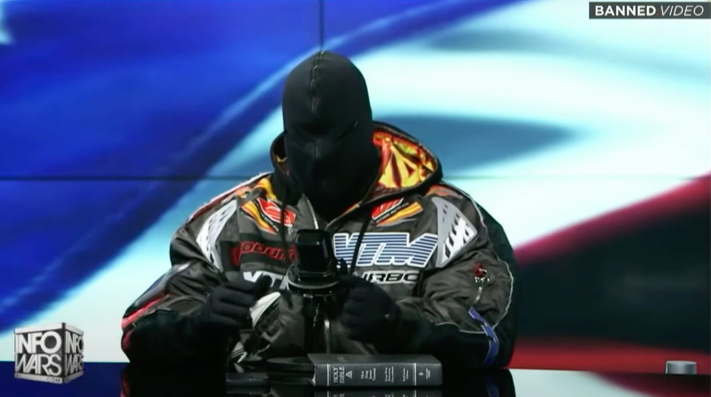 Kanye West wearing a puffer jacket and a mask hood covering his entire head, on the set of the Alex Jones Show.