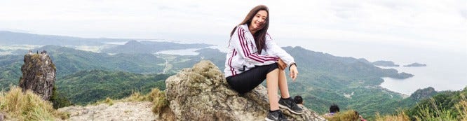 A girl smiling a view of the green mountains and ocean