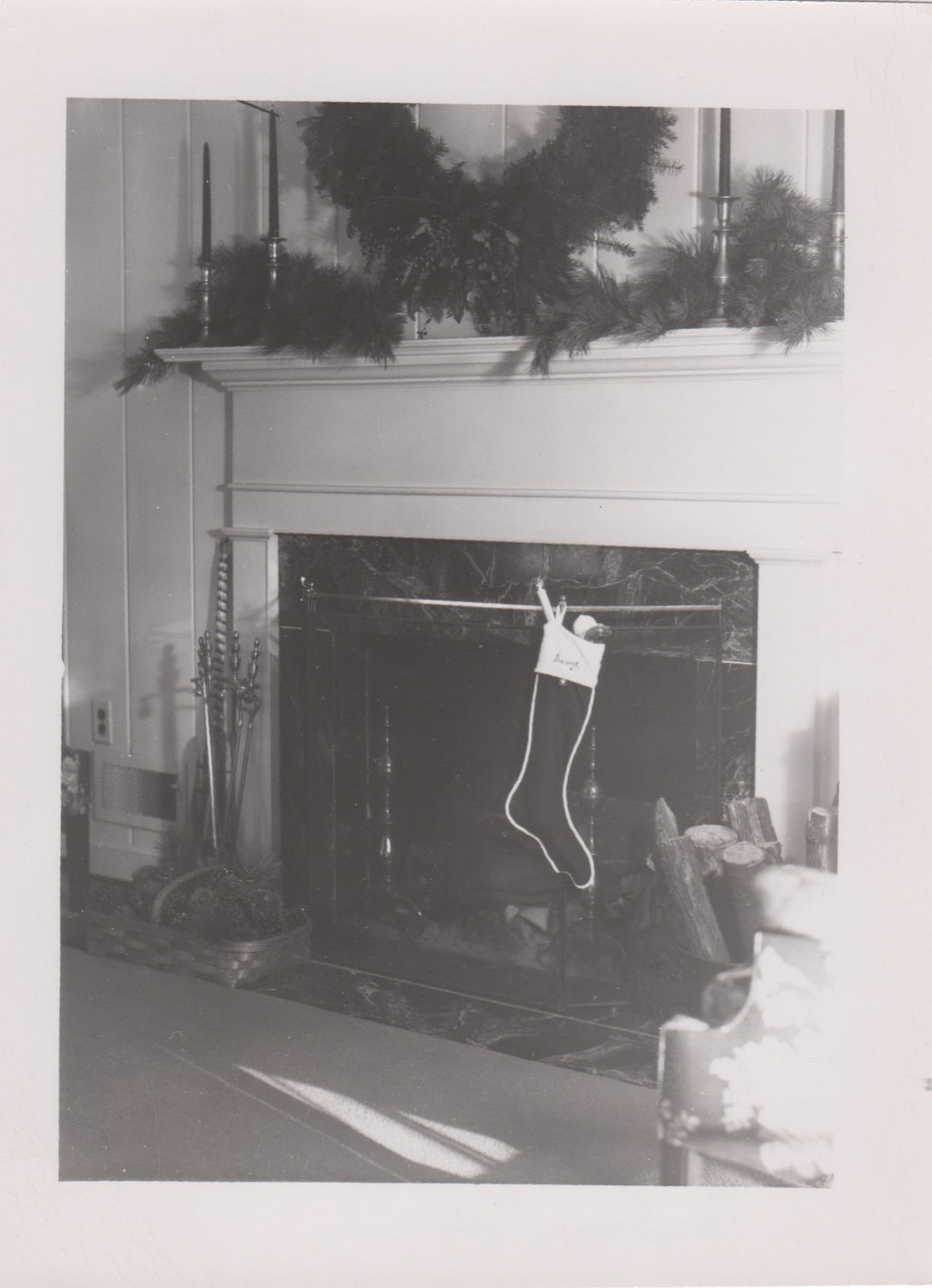 Photo of hearth decorated for Christmastime, with a large evergreen wreath above the mantle and fluffy evergreen branches on the mantle.
