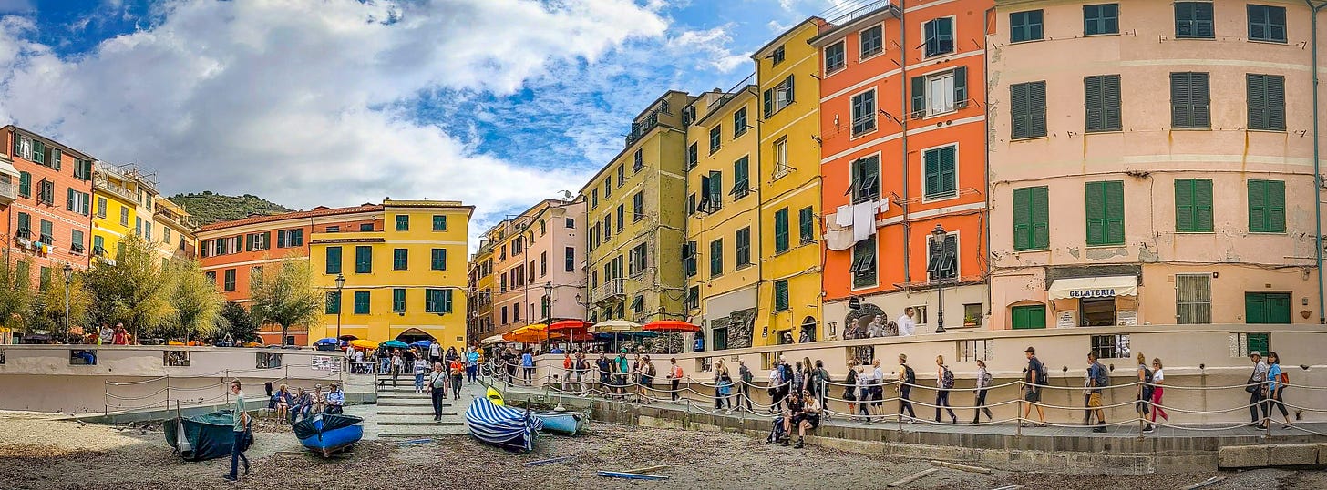 A photo from near the water looking back up at the pastel-colored buildings of Vernazza. 