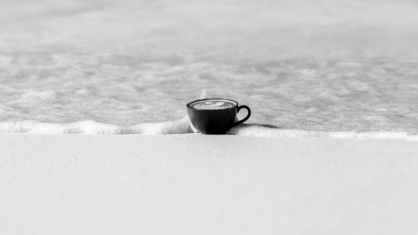 A cup of coffee on a beach at the edge of the waves