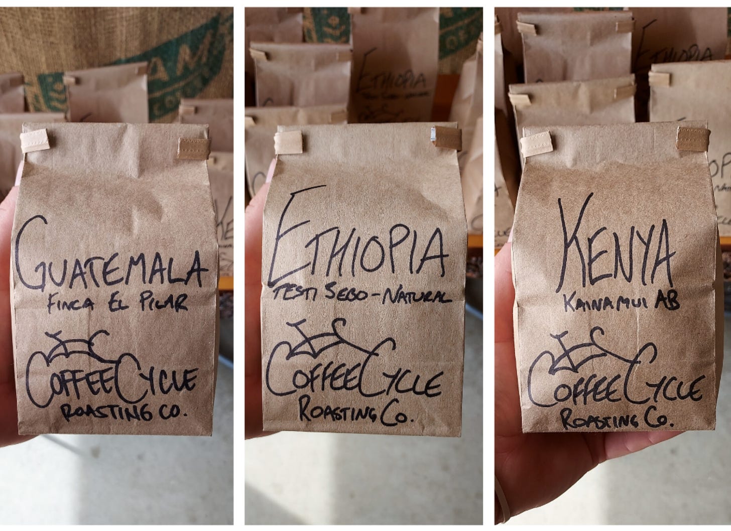 Three side by side images of brown paper coffee bags with a Coffee Cycle bicycle logo drawn on with black sharpie, and the coffee origin-Guatemala, Ethiopia, Kenya-above the logo. The bags are held up close to the camera and blurred out bags are seen in the background.