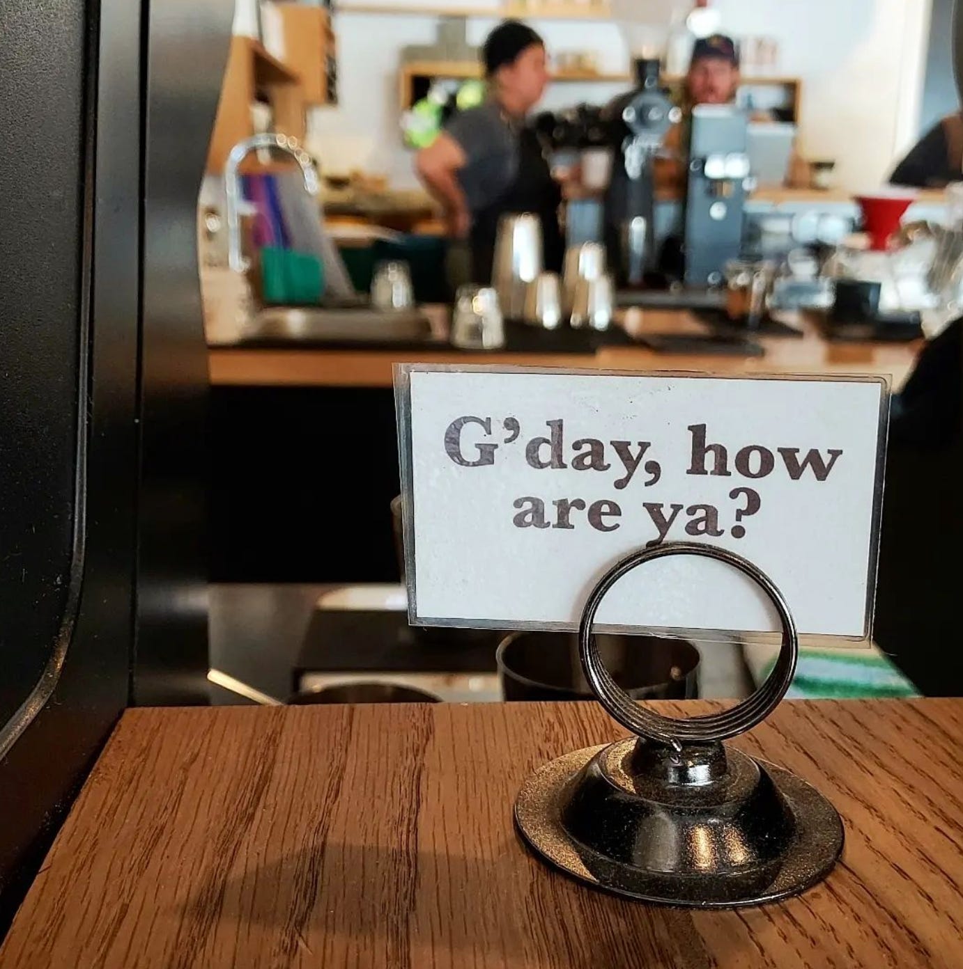Close up on a sign on a cafe counter that says, "G'day, how are ya?"