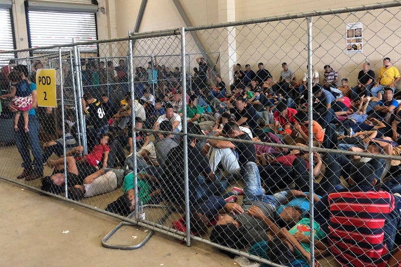 Parents and children sitting on the floor, crowded into a cage inside the detention facility.