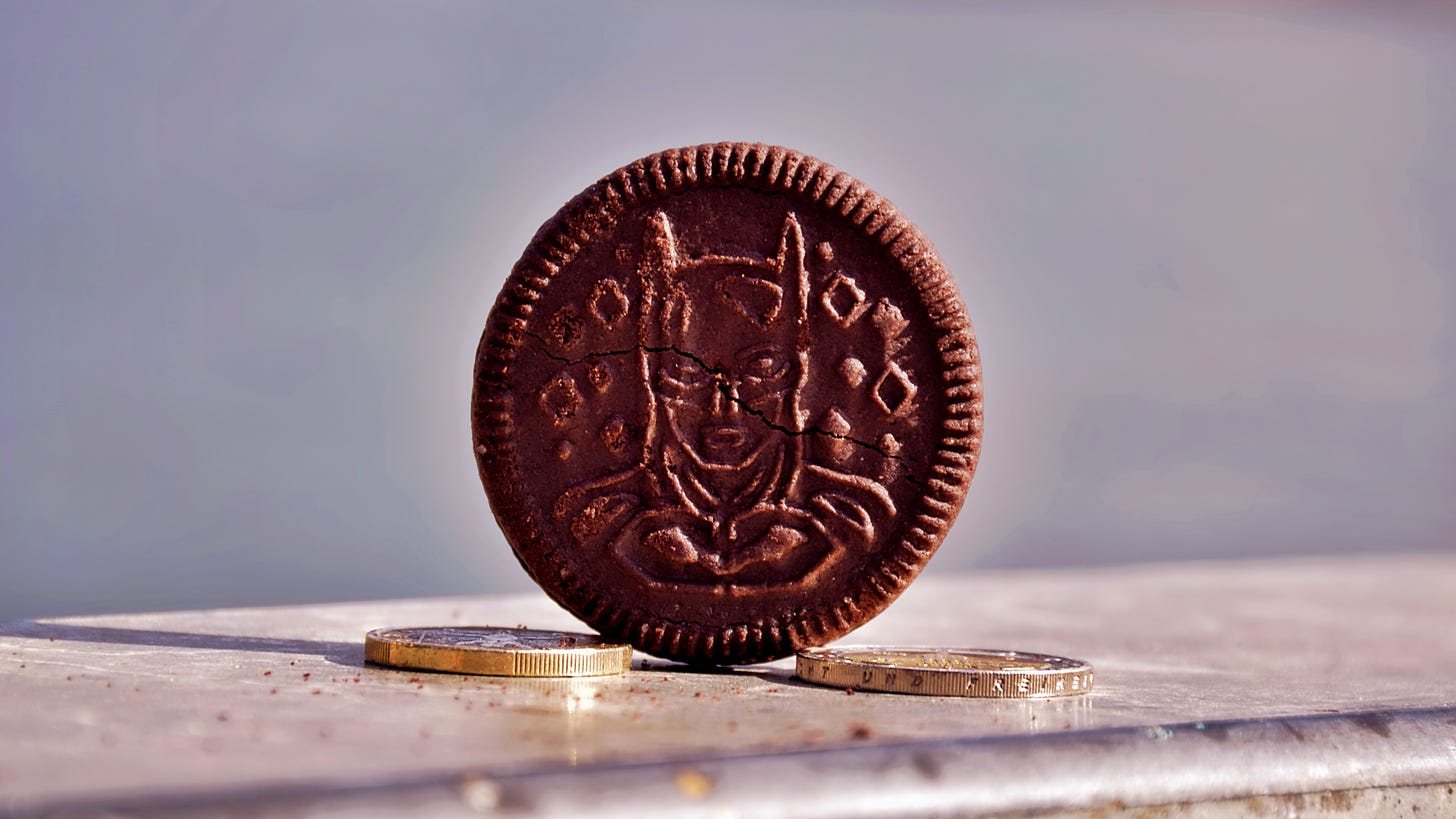 An upright Oreo with The Batman-designed face, two two-euro coins lain on either side on steel surface