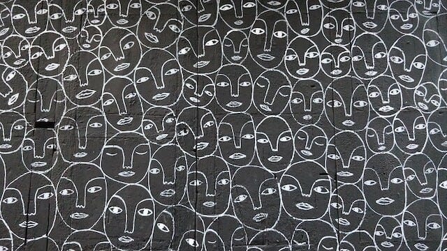 repeated faces drawn in white chalk over a black surface