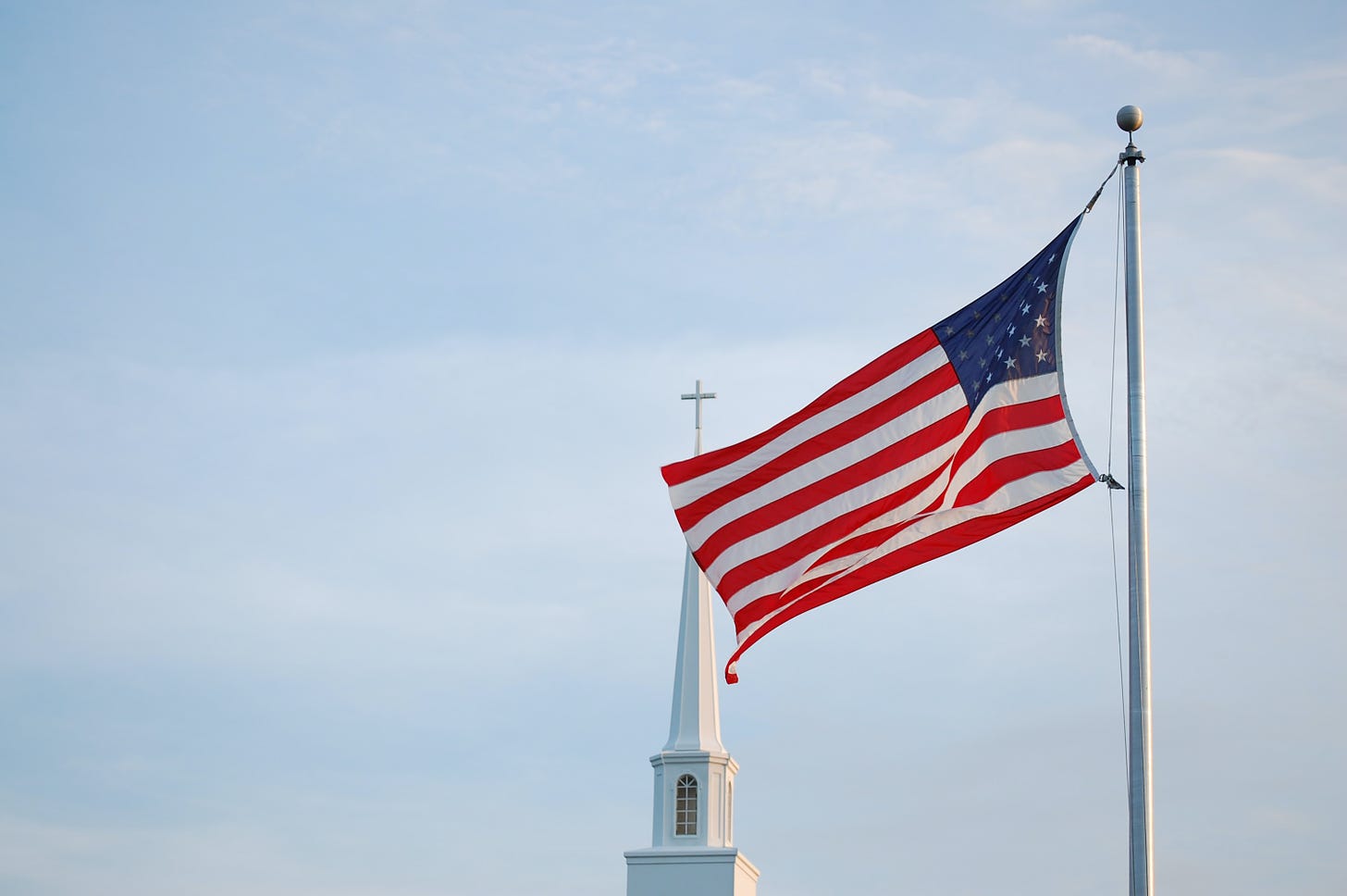 Blue sky background with american flag on flag pole and church steeple in foreground