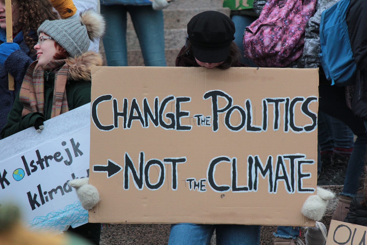 A protester at a rally is holding a cardboard sign, "Change the politics, not the climate"