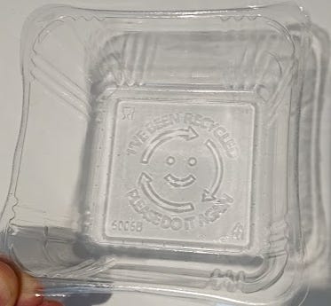 Plastic container with embossed text saying 'I've been recycled, please do it again' and a smiley face.