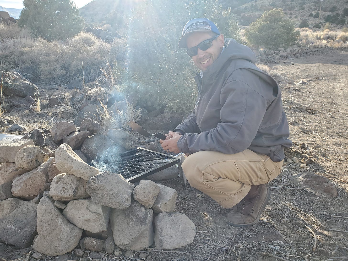 Eric squatting in front of a DIY grill supported by rows of rocks.