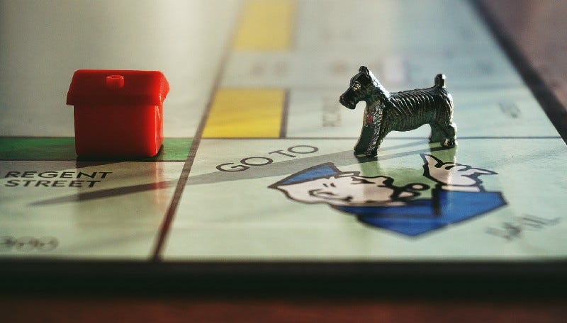 A Monopoly board game, with a pewter dog facing a red plastic house.