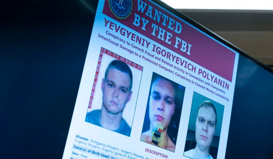 Russian Yevgeniy Polyanin, wanted by the FBI, is displayed on monitors as Attorney General Merrick Garland accompanied by Deputy Attorney General Lisa Monaco and FBI Director Christopher Wray speaks at a news conference at the Justice Department in Washington, Monday, Nov. 8, 2021. (AP Photo/Andrew Harnik)