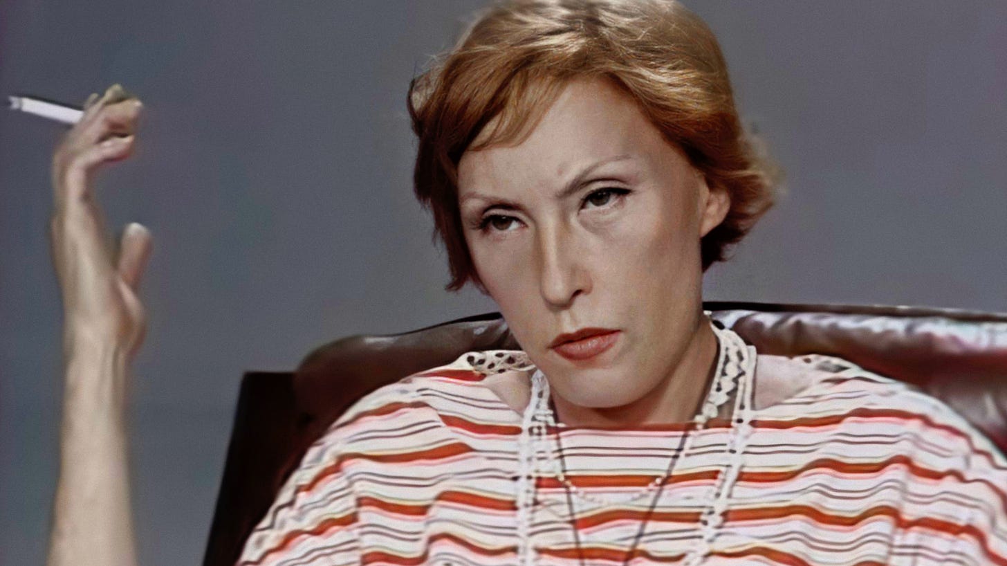 fotografia de Clarice Lispector na entrevista do programa Panorama, séria, olhando para o entrevistador, usando um vestido listrado, vários colares, segurando um cigarro com a mão direita na altura do rosto