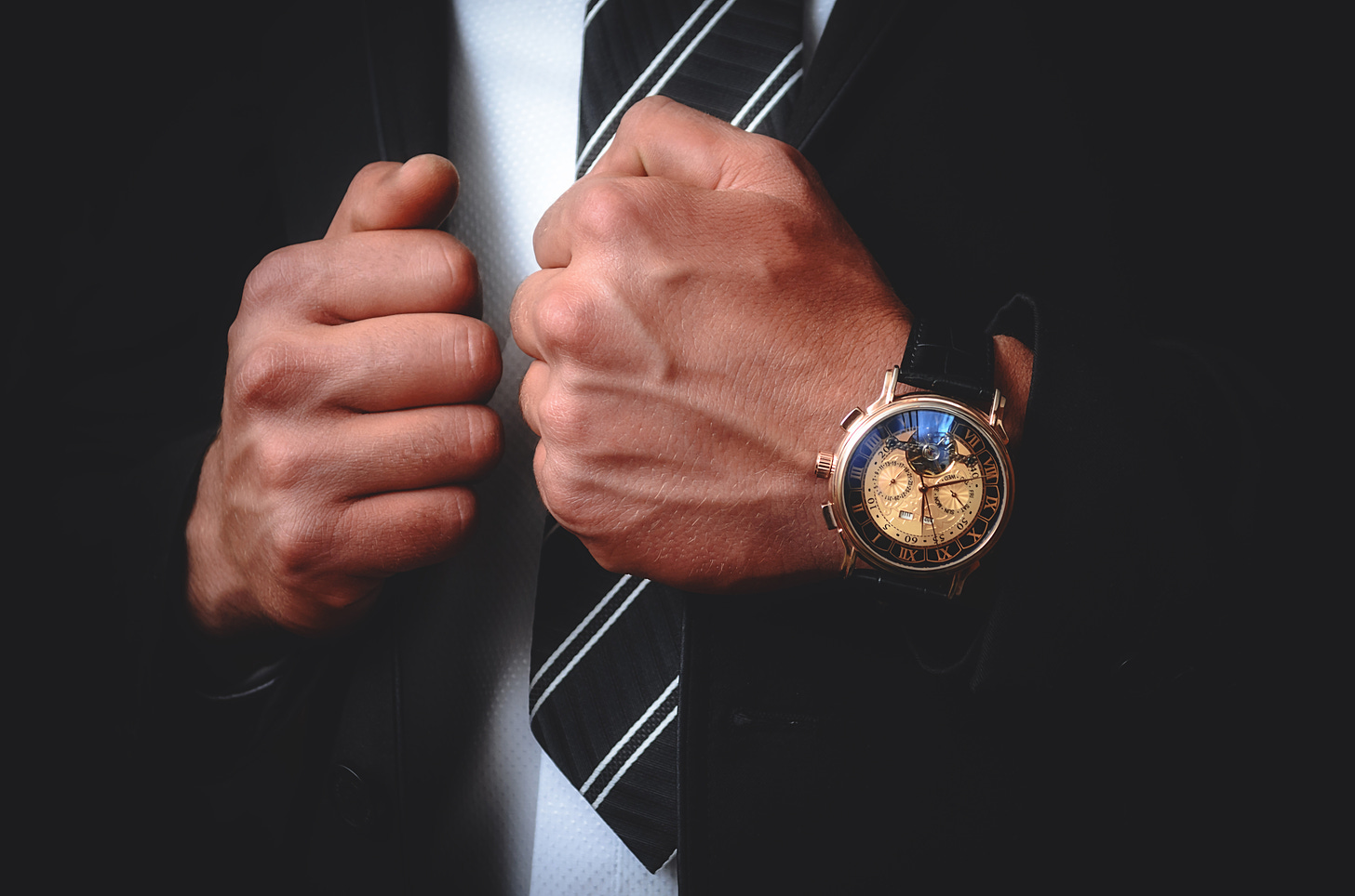 Man in suit with diagonal striped tie and elaborate watch that looks like it has  multiple time zones. I'm not sure. I'm not the watchmaker to the King.