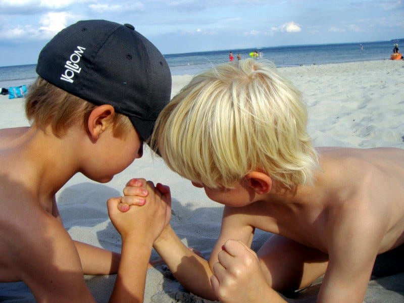 Two boys arm wrestling on beach.