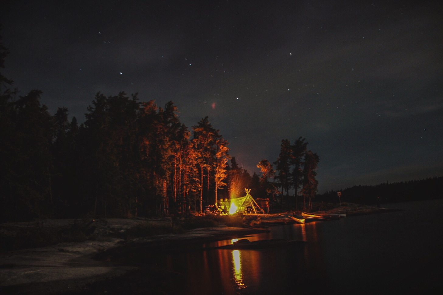Campfire on the edge of a lake underneath a starry sky