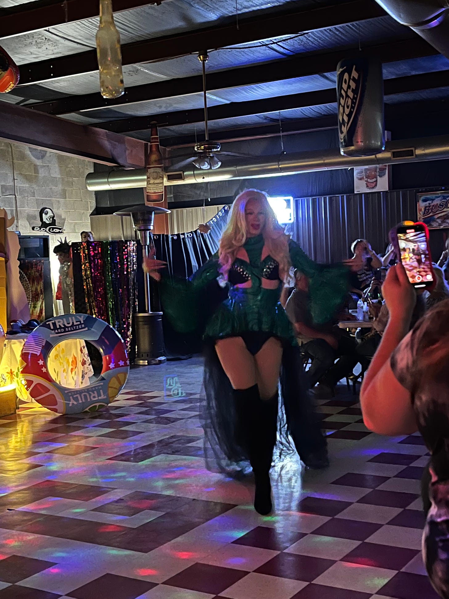 A drag queen with blonde hair an a green cut-out outfit struts during her performance at Good Times Bar.