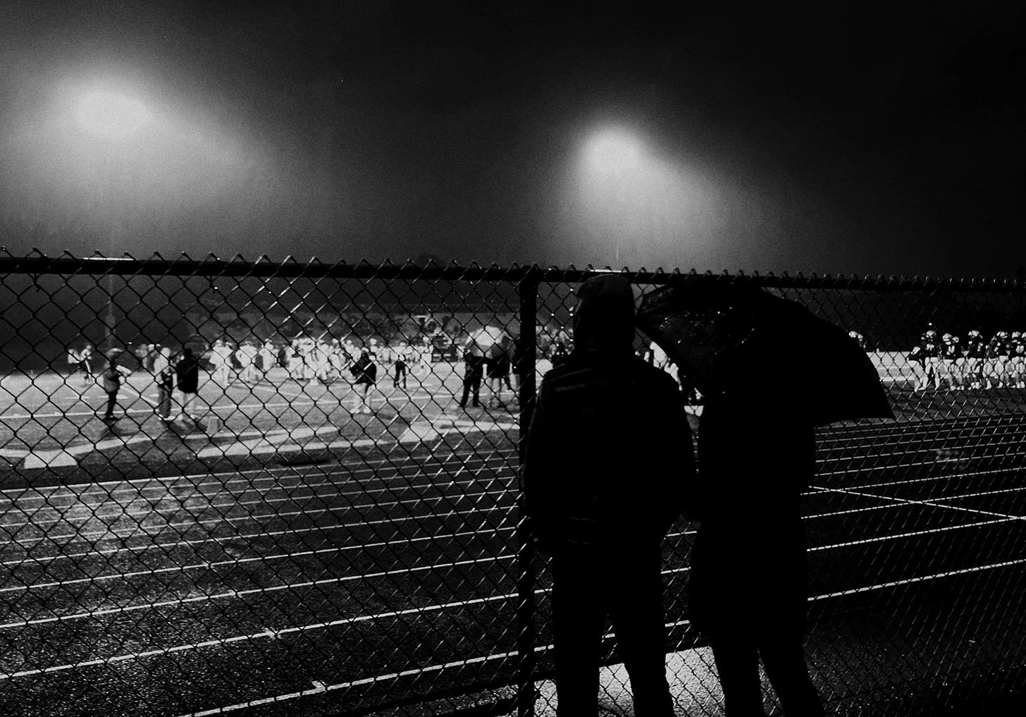 A couple watches the football game from behind the ground level fence near the field.