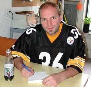 Man in a Pittsburgh Steelers jersey sitting with a pen and pad of paper.