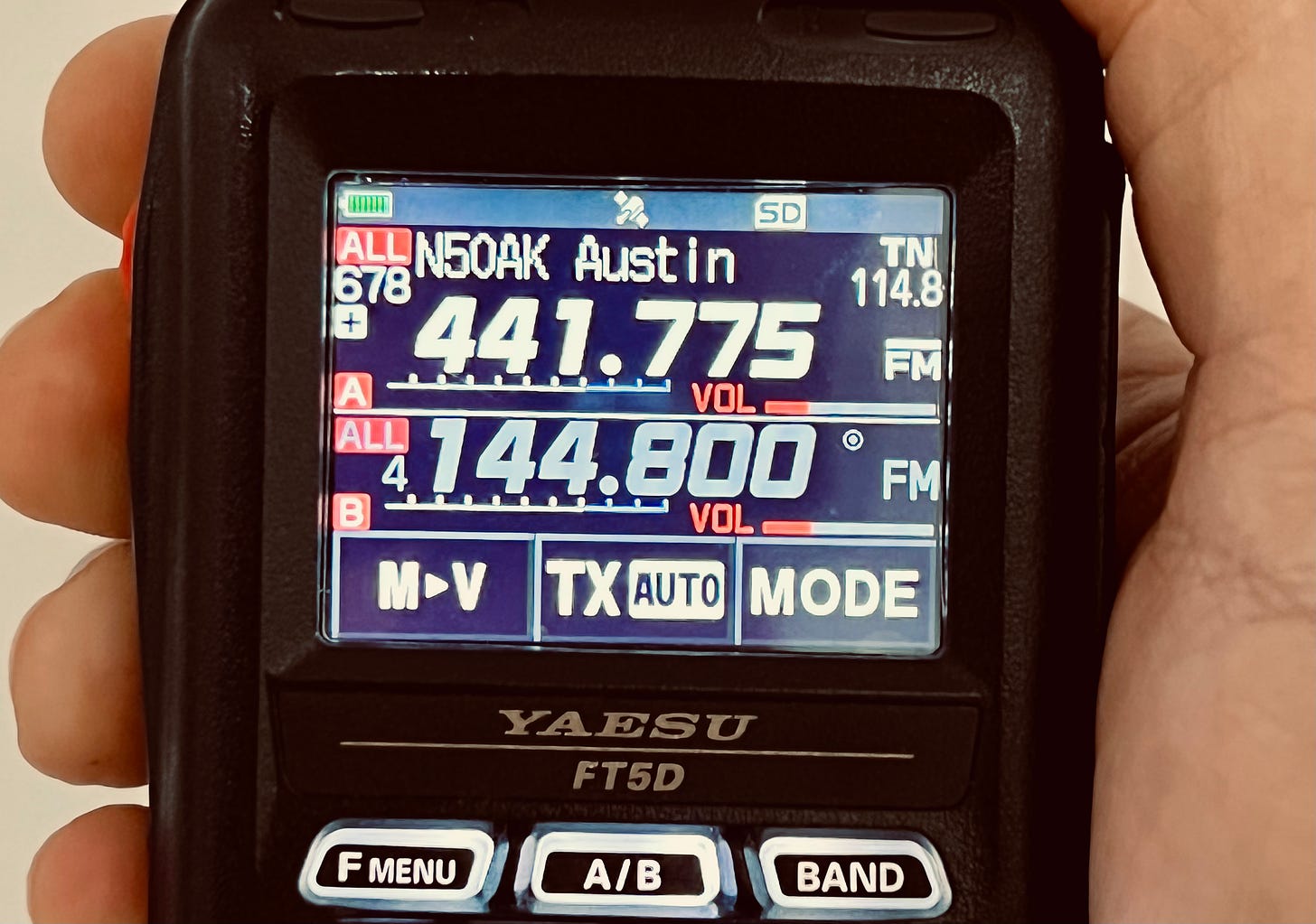 A hand hold a Yaesu FT5D with the frequency for the repeater N5 OAK visible on the screen