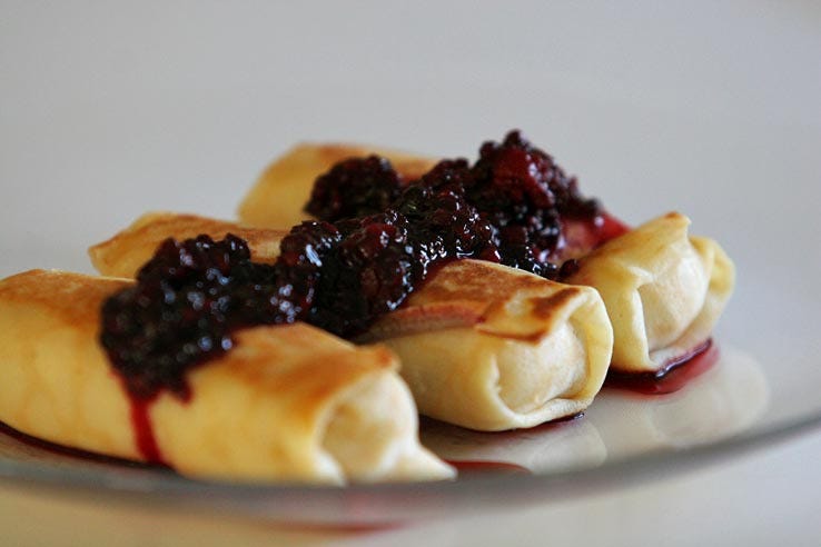 Image of three blintzes on a white plate, covered in blackberry compote.