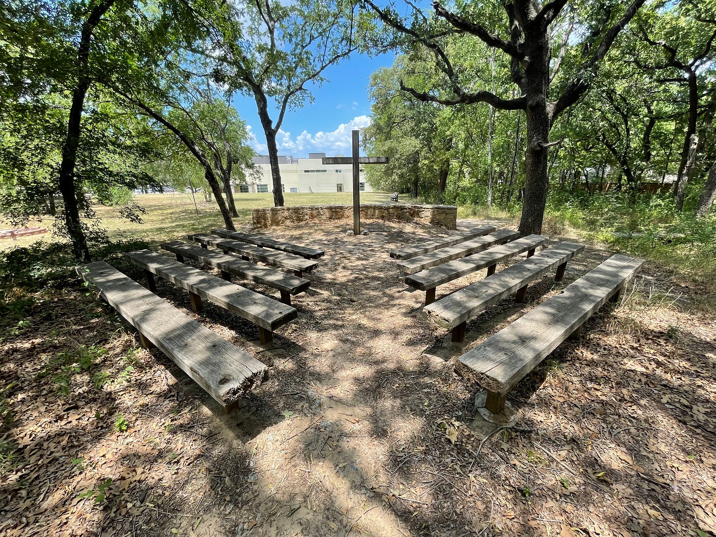 Eight shaded benches facing a wooden cross