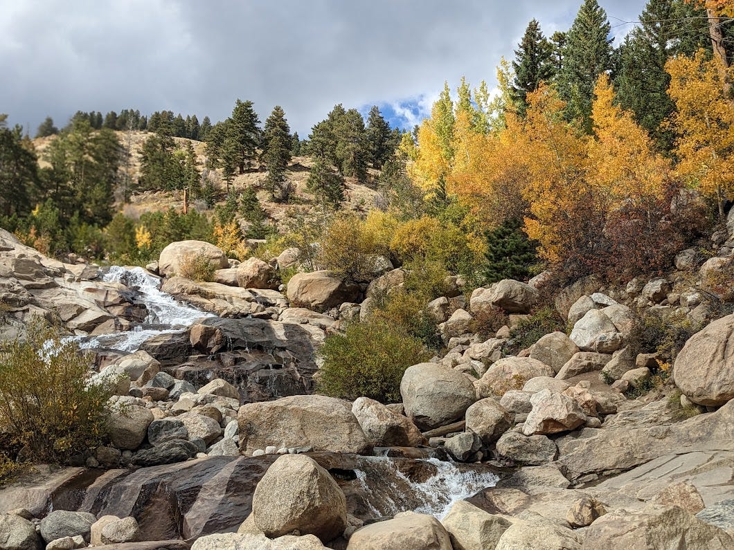 Alluvial fan at Rocky Mountain National Park, showing a portion of a waterfall flowing down boulders surrounded by green pines and golden aspens