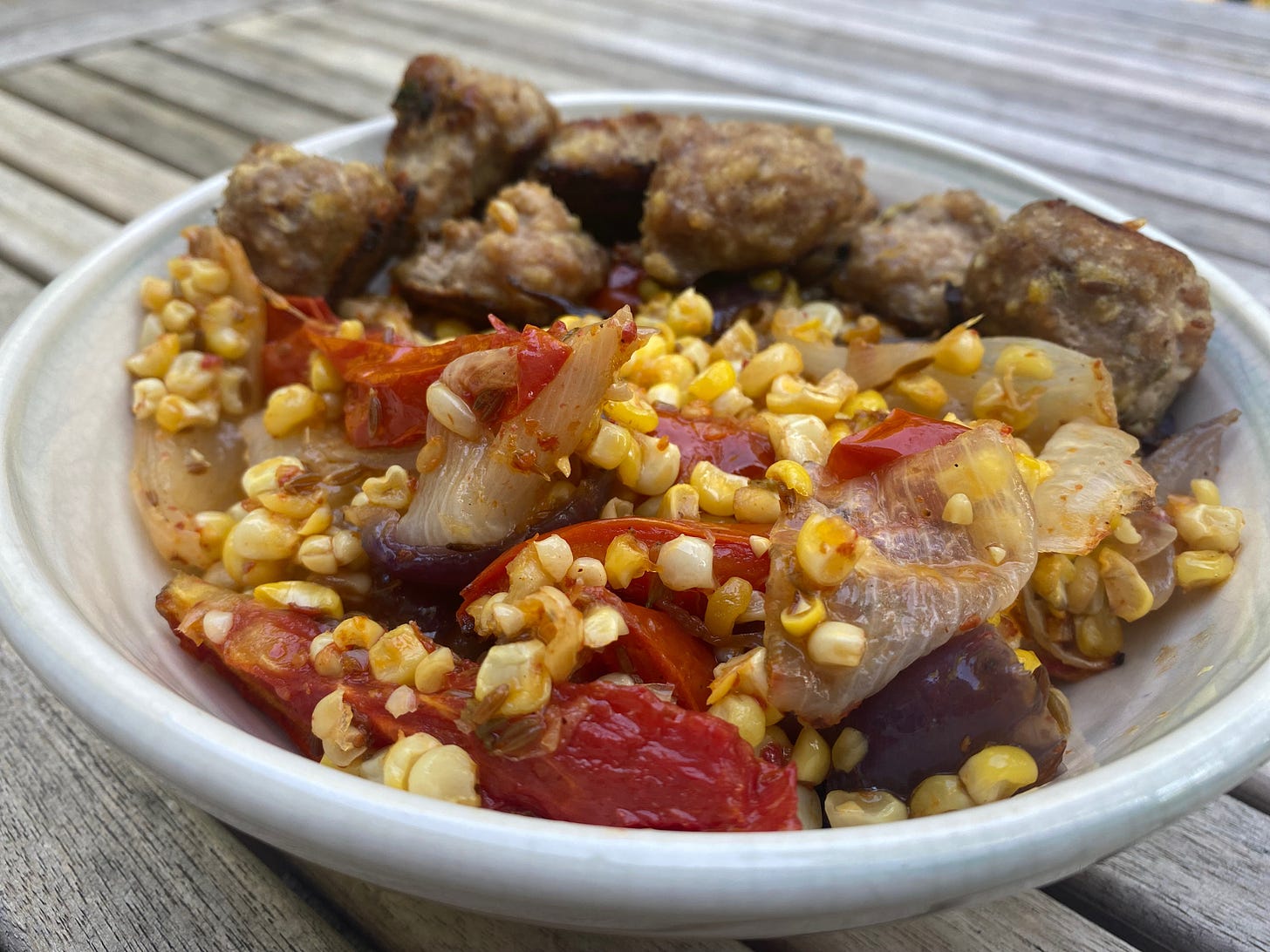 A ceramic bowl full of roasted corn, onions, and tomatoes with meatballs piled along one edge.