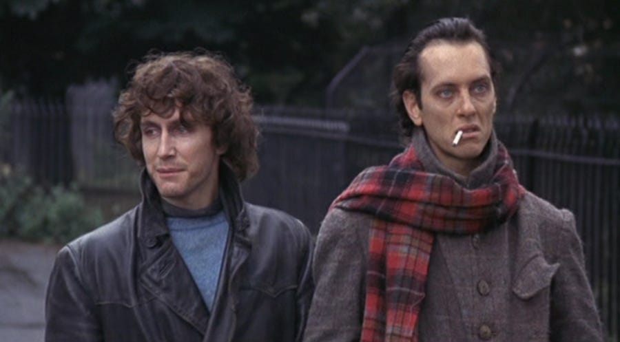 left: paul mcgann as i, with messy hair and a leather jacket; right: richard e grant as withnail, with a cigarette, a tartan scarf, and a grey coat, looking gaunt. they're walking through regent's park.