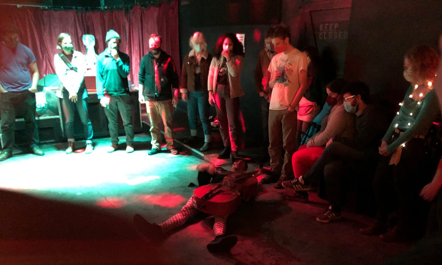 A man lying on his back while playing the cello as a circle of audience members watches A man lying on his back while playing the cello as a circle of audience members watches