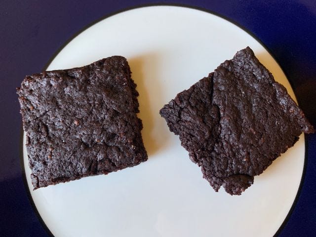 Two dark brownies on a white plate with a blue rim.