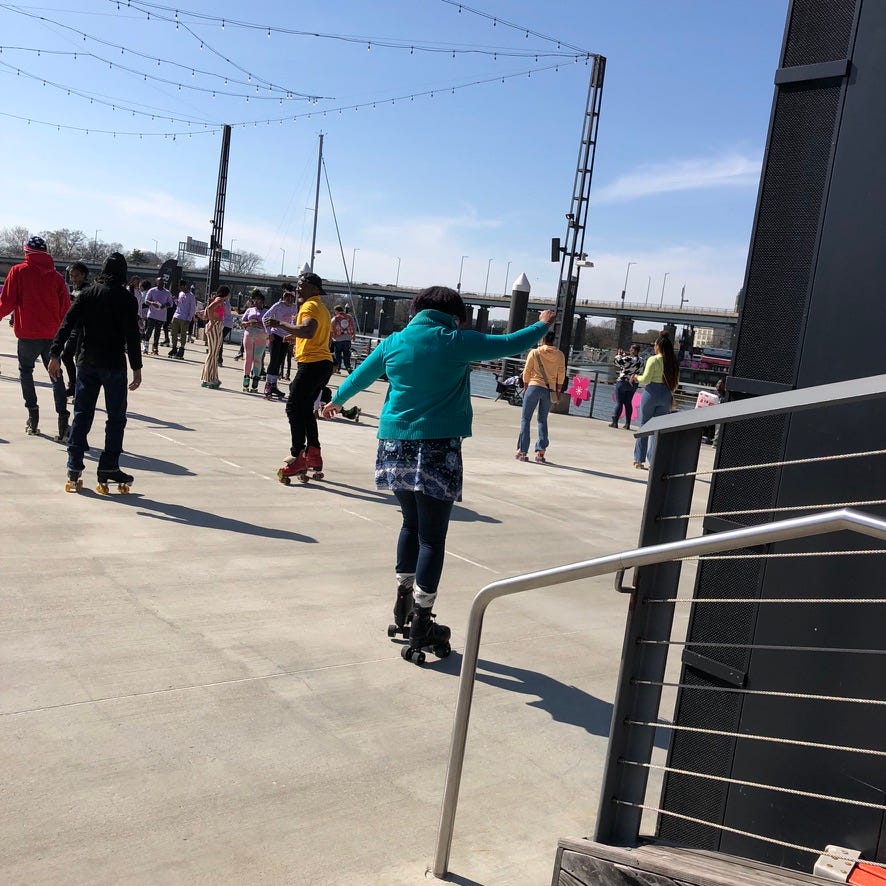 A group of skaters outside on a pier in DC. Kristen is in the foreground in a green jacket turning a corner on her skates