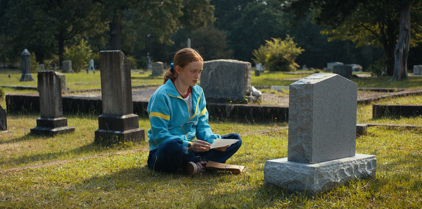 Max sits in front of a gravestone in Stranger Things season 4