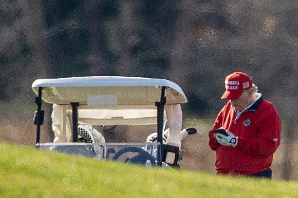 Former President Trump checks his phone on a golf course