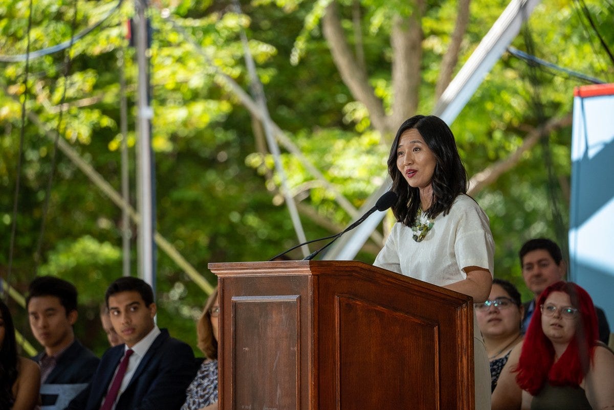 Mayor Michelle Wu speaks at a wooden podium while students look on.