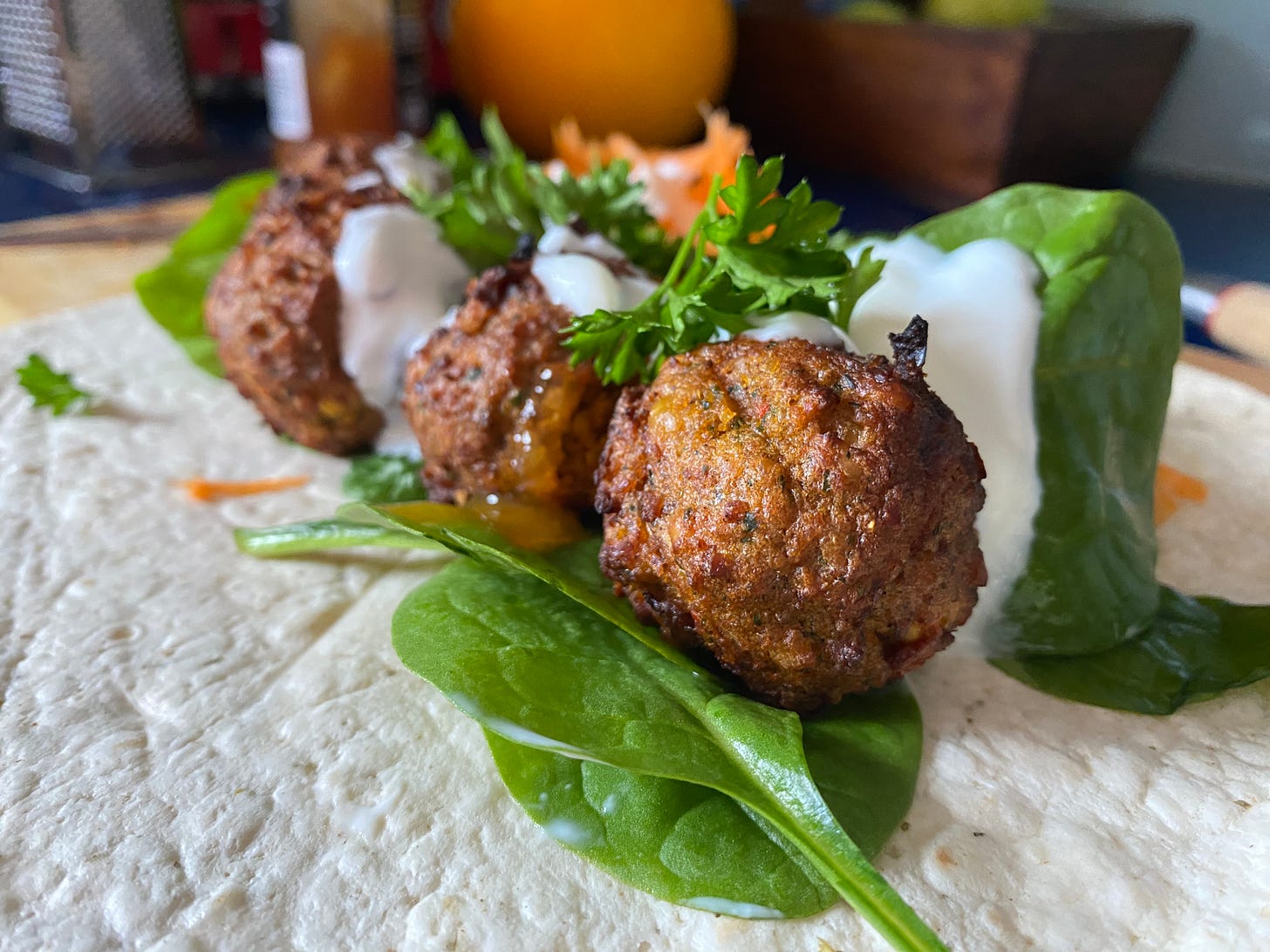 Tortilla wrap, topped with spinach leaves, falafel, yoghurt, grated carrot and fresh parsley