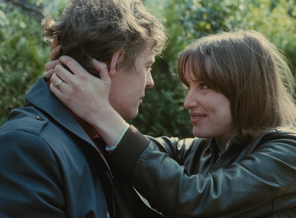 Movie still from Love in the Afternoon. A couple look into each other's eyes outside. The woman holds the man's face in her hands.