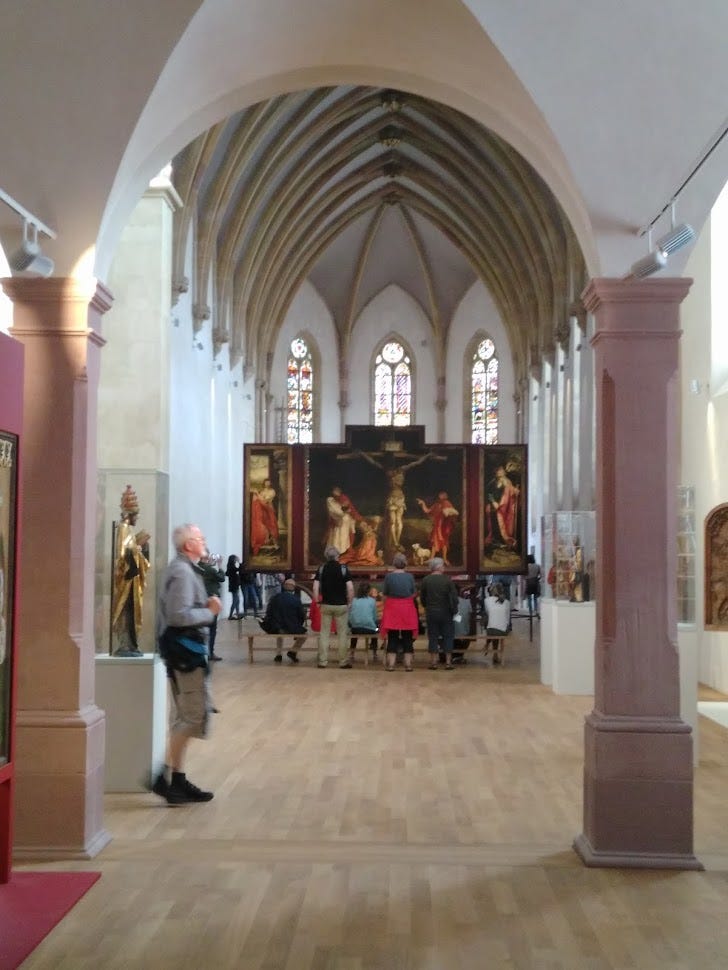 The painting with the old priory church around it.  People are looking up at it, and the figures in the painting are life-size or larger.