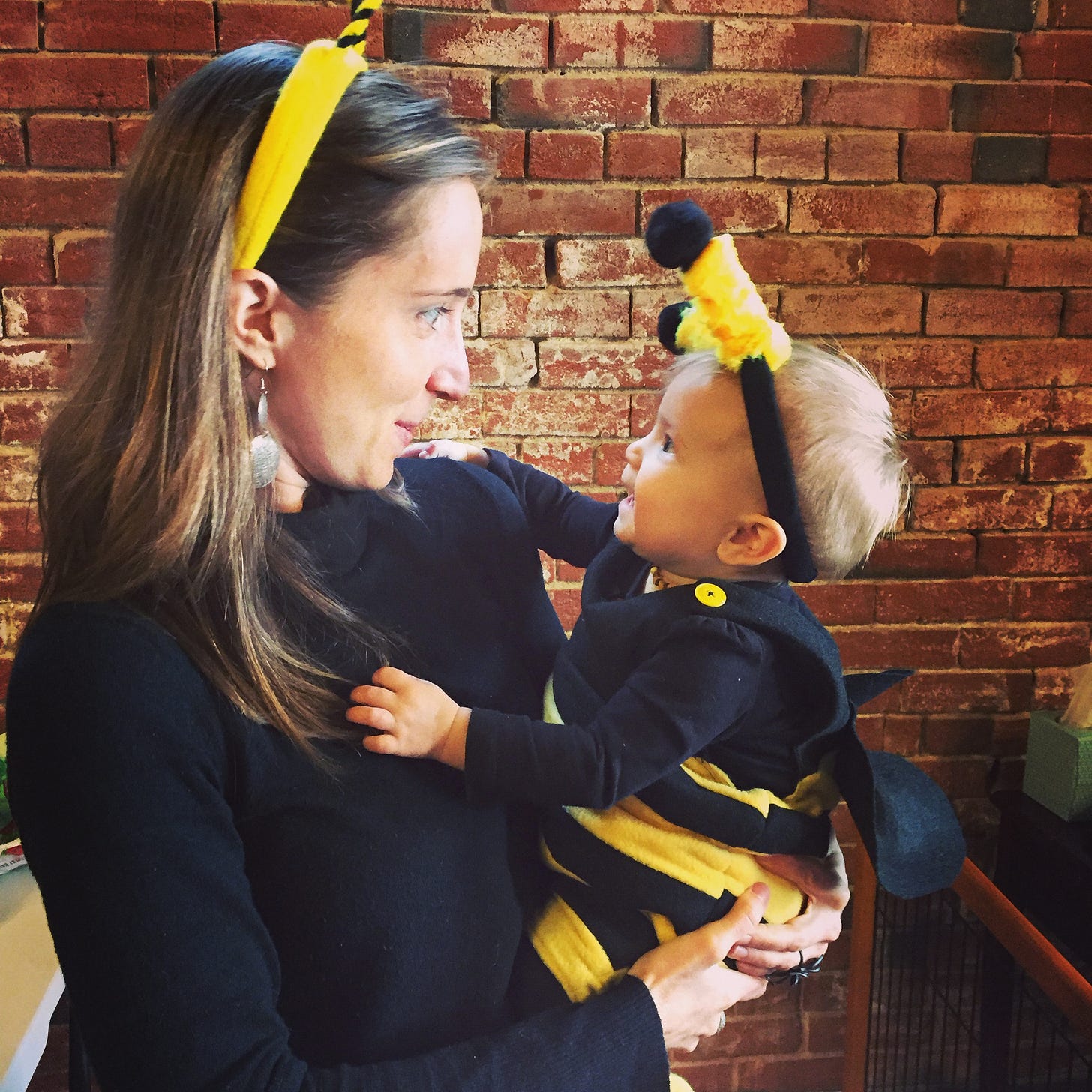 Kari, dressed in all black with bee antenna headband holds a baby in a matching costume