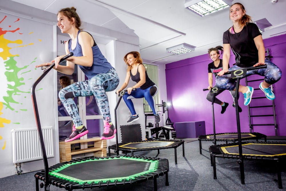 Group of women happily exercising on hexagonal trampolines with stability bars