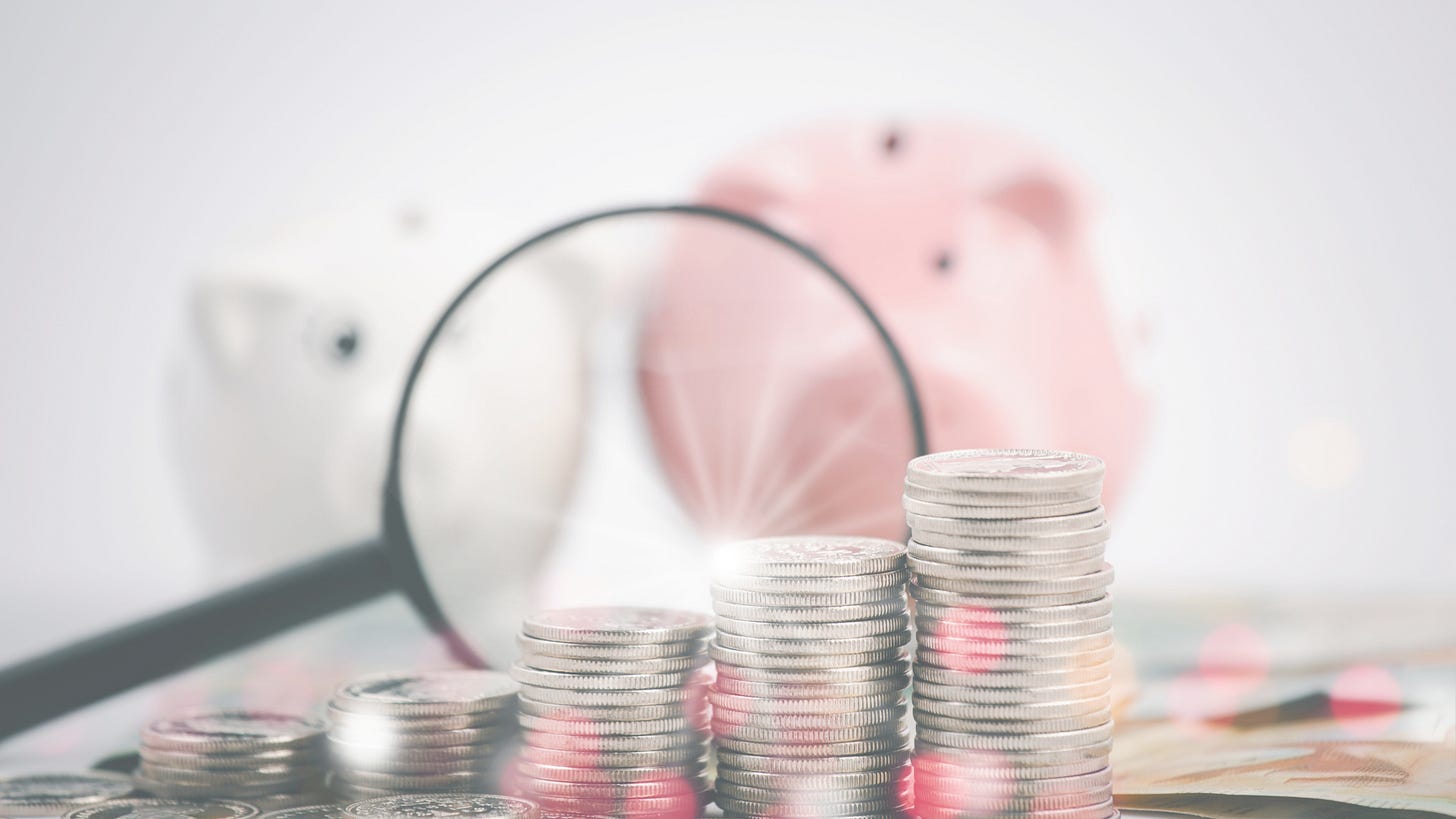 Magnifying glass with coins and piggy bank in background