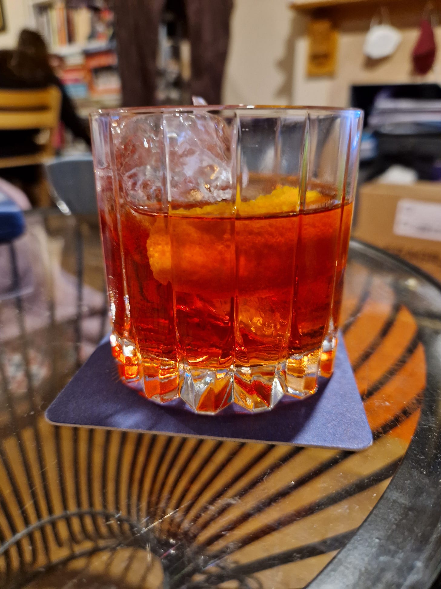 A glass holding a negroni cocktail, on a coaster, on a glass-topped table.