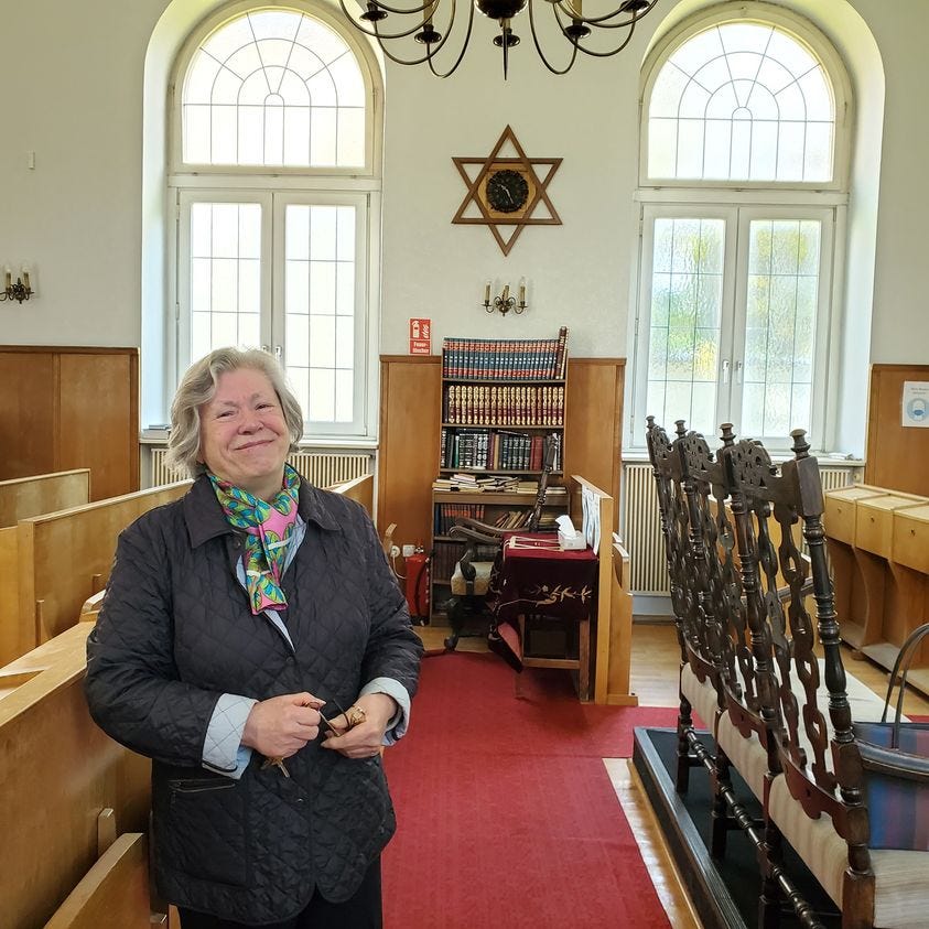 A white woman stands in the middle of a small Jewish synagogue. 