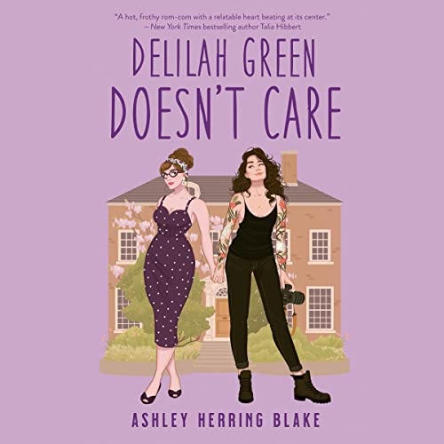 The audiobook cover of Delilah Green Doesn’t Care: an illustration of two white women standing in front of a house. One is wearing a polka-dotted dress; the other a black jumpsuit that reveals her tattooed arms.