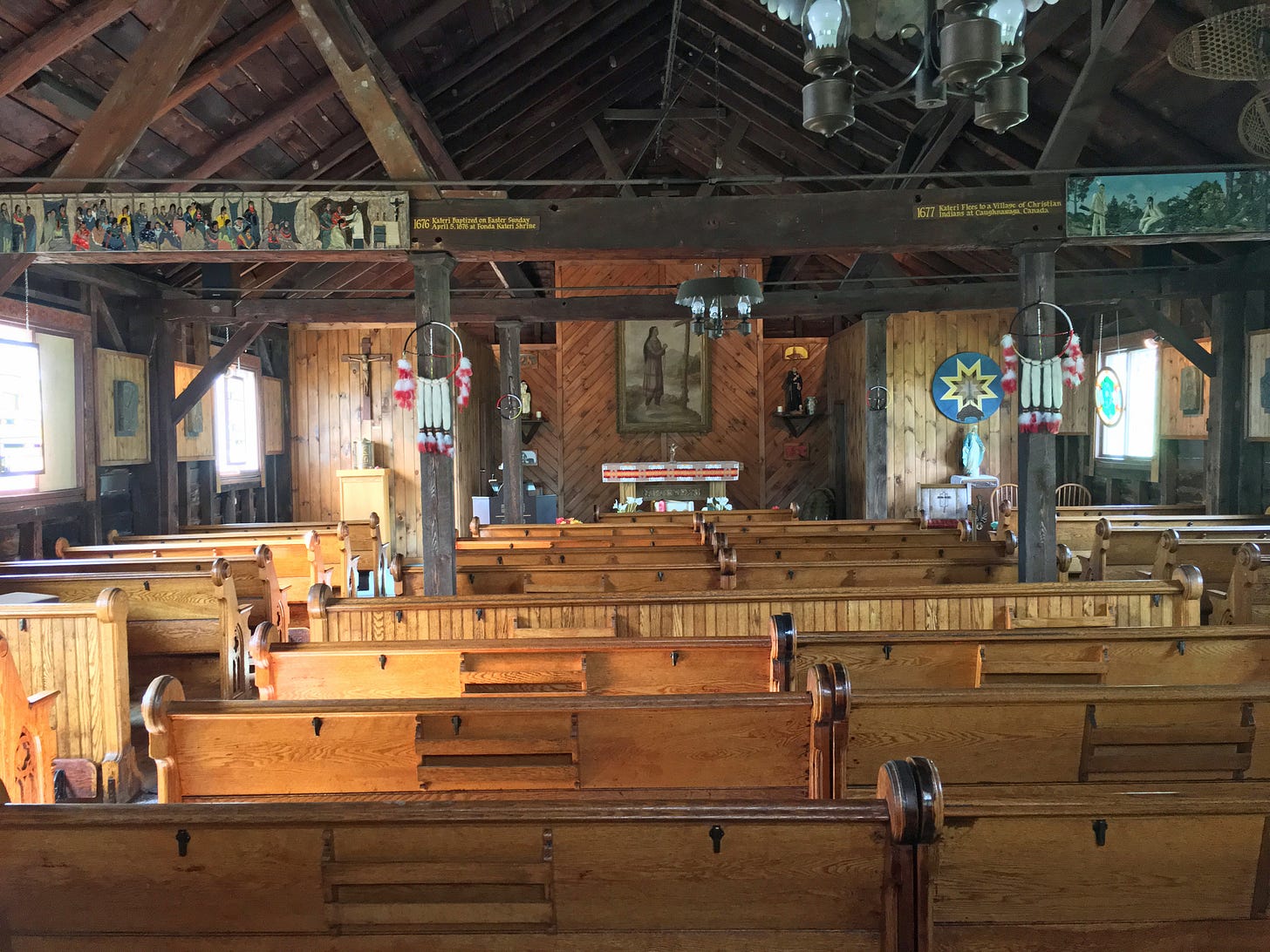 Interior of a rustic church hung with Catholic icons, Native American totems, and depictions of Kateri Tekakwitha.
