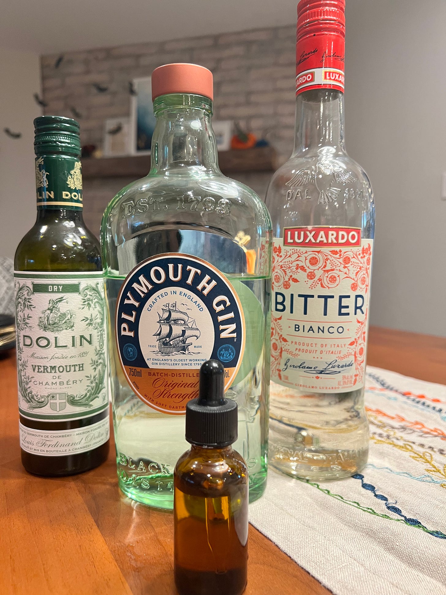 Bottles of the 4 ingredients in the cocktail: Plymouth Gin, Dolin Dry Vermouth, Luxardo Bitter Bianco, and saline solution
