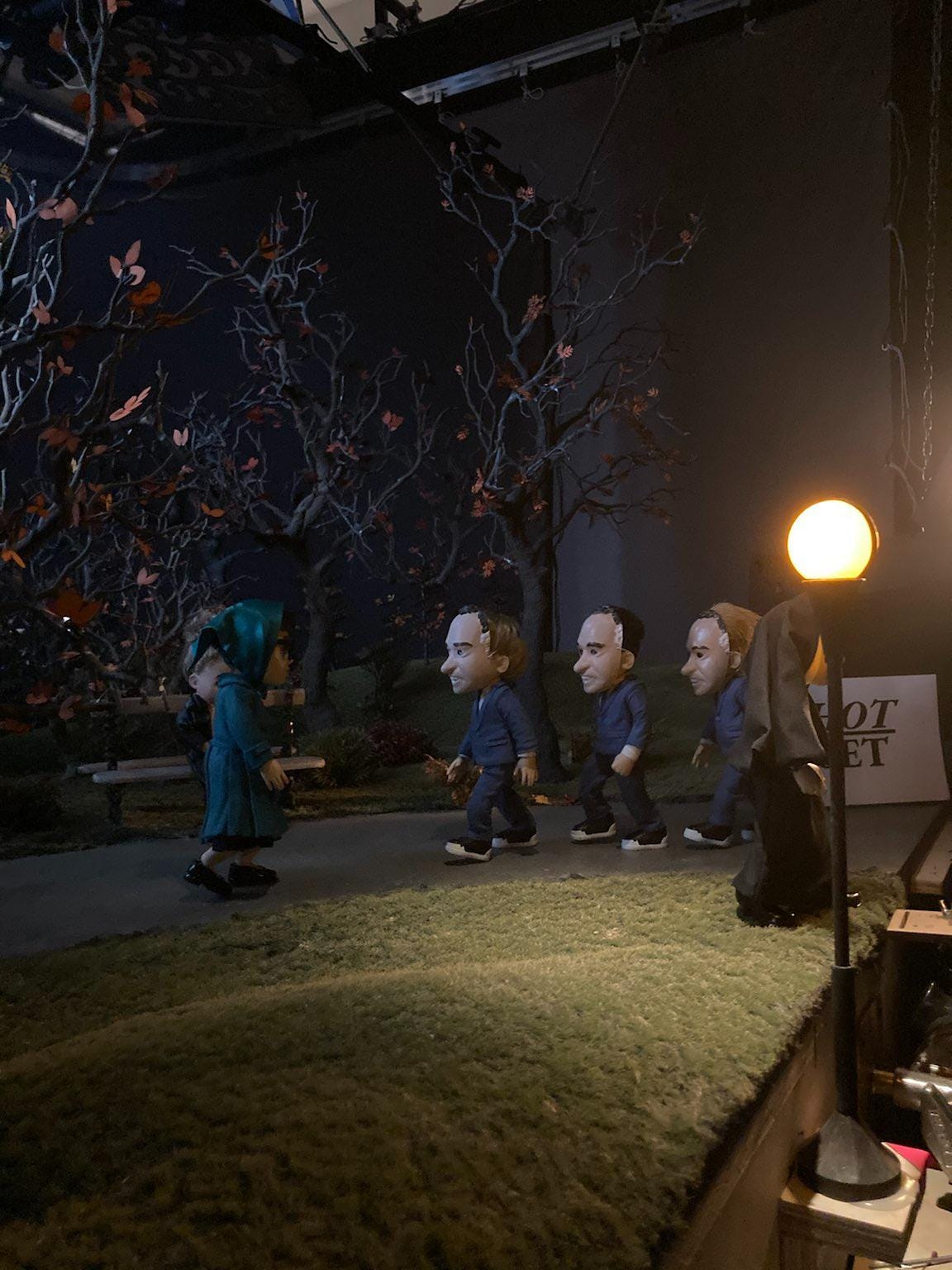4 puppets are walking in a stop motion miniatrure set modeled after NYC's central park. 3 of the characters have "Nixon masks" on that are super creepy. The 4th character is walking towards the group, she is wearing all teal and sunglasses and looks like she has many secrets under her headwrap.