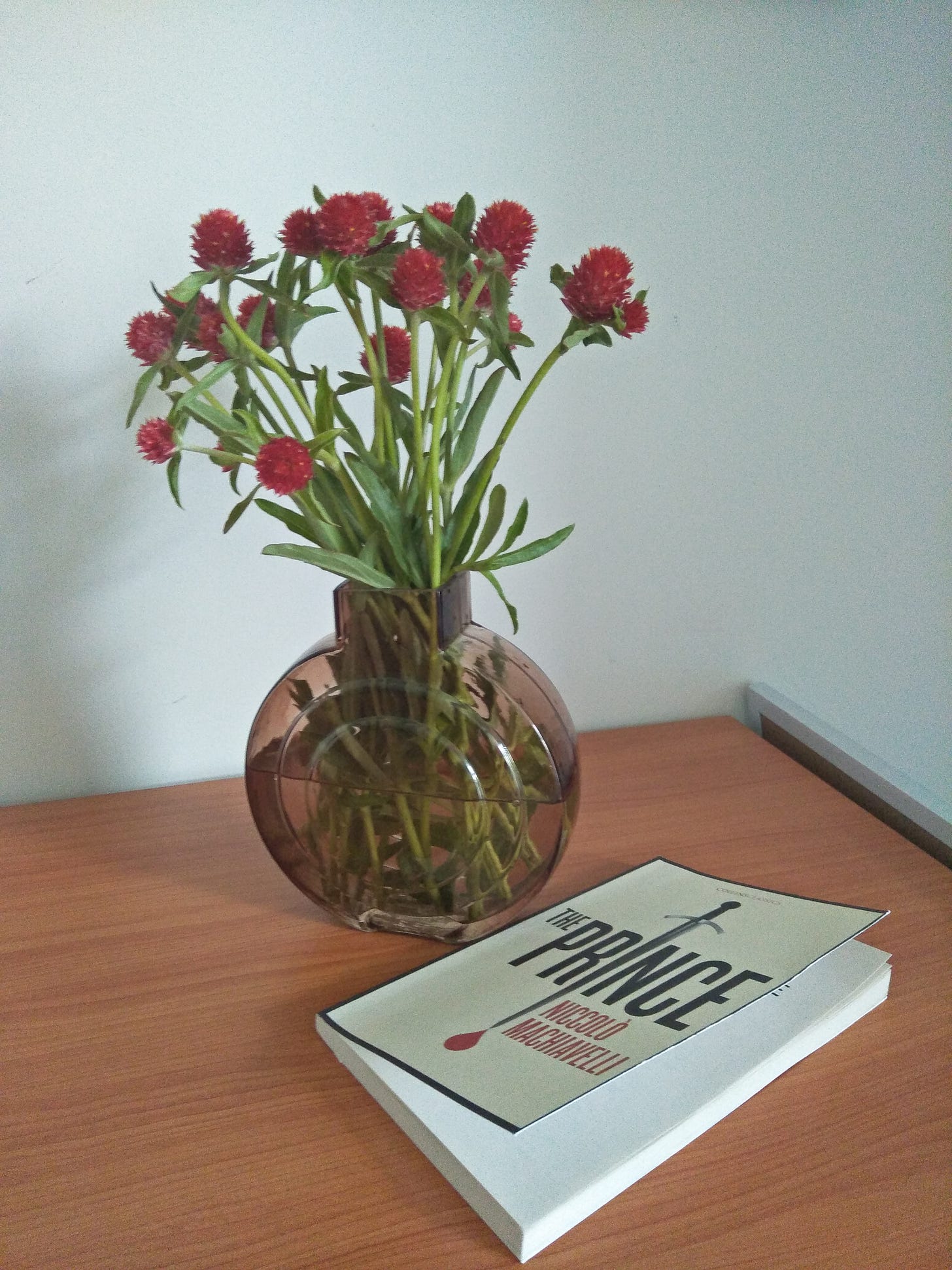 Art deco vase folding Strawberries Fields flowers next to a paperback copy of Machiavelli's "The Prince"